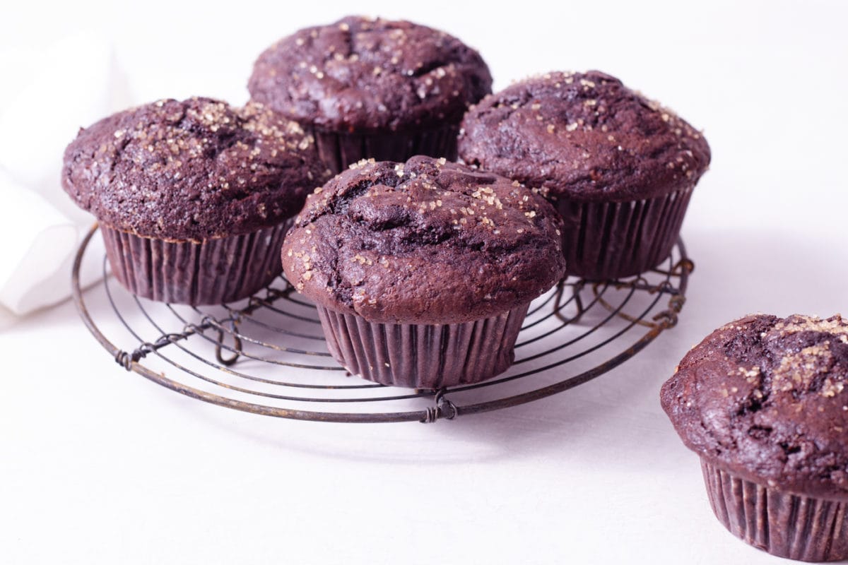Straight on shot of Chocolate Muffins with chocolate chips on a wire rack on a white surface.
