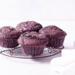 Straight on shot of Double Chocolate Chip Muffins on a wire rack on a white surface.