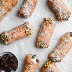 Overhead view of cannoli with ricotta mascarpone filling decorated with pistachios and chocolate chips.