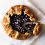 Overhead shot of a lavender blueberry galette on parchment paper on a light, textured background.