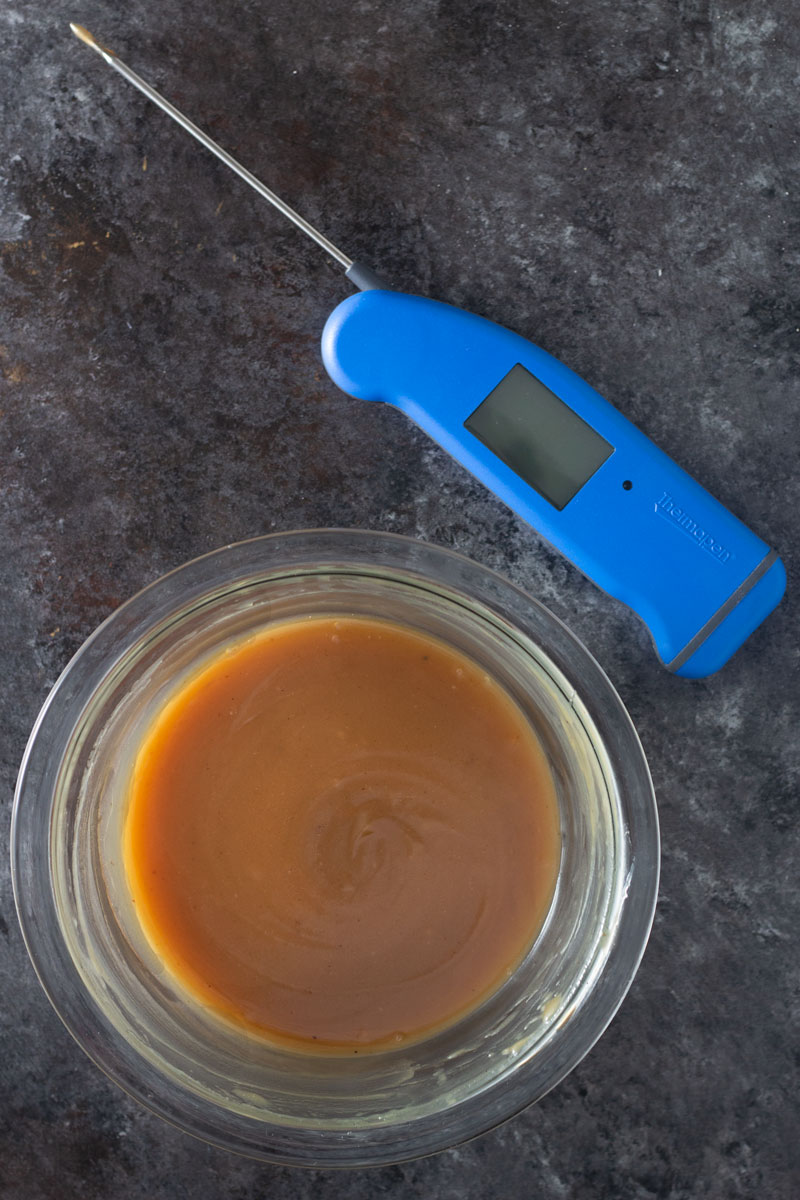Overhead shot of a bowl of tamarind salted caramel sauce next to a Thermapen thermometer on a dark, rustic textured background.