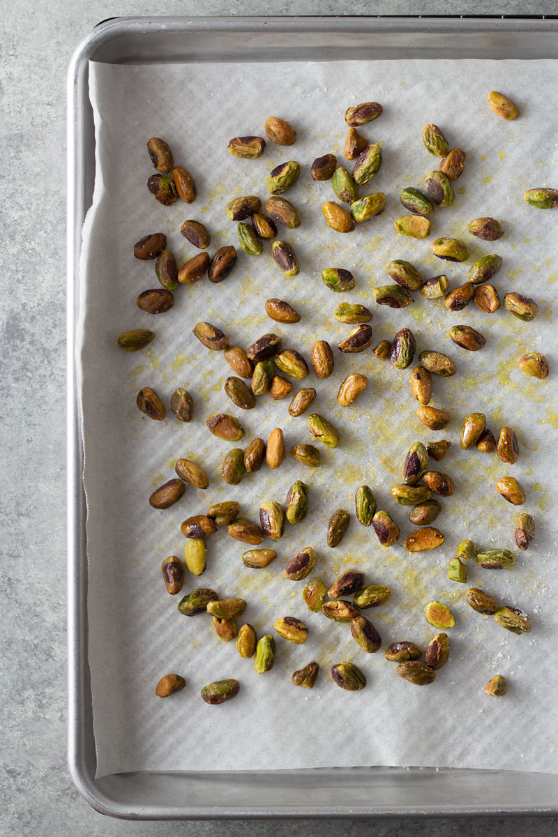 Overhead shot of buttery, salted pistachios on a parchment lined sheet tray after toasting.