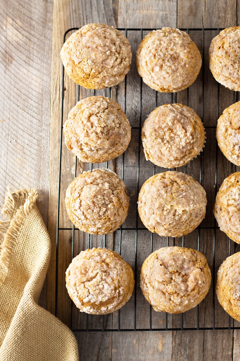 Overhead shot of a rack of Pumpkin Cream Cheese Streusel Muffins on a grey wood surface surrounded by a tan cloth.