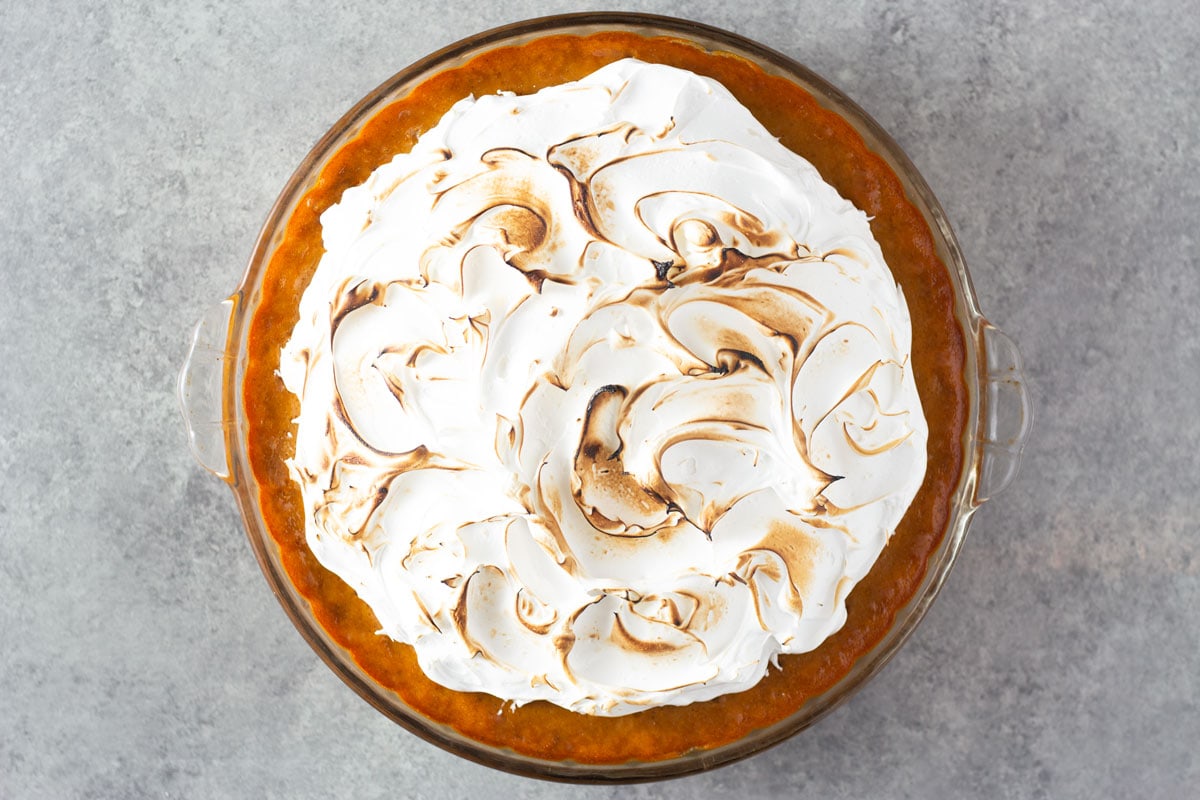Overhead shot of a pumpkin meringue pie with pecan graham crust on a light grey, textured surface.