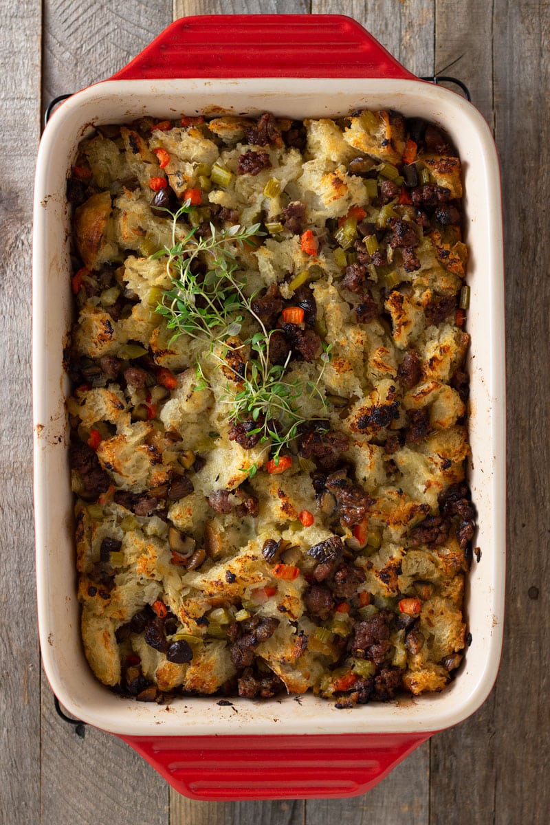 Overhead view of a red baking tray of Sausage Chestnut Stuffing topped with fresh thyme on a grey wood surface.