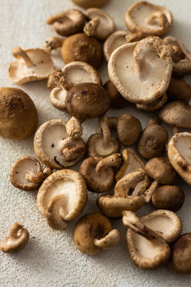 ¾ angled shot of raw baby shiitake mushrooms on a white textured surface.