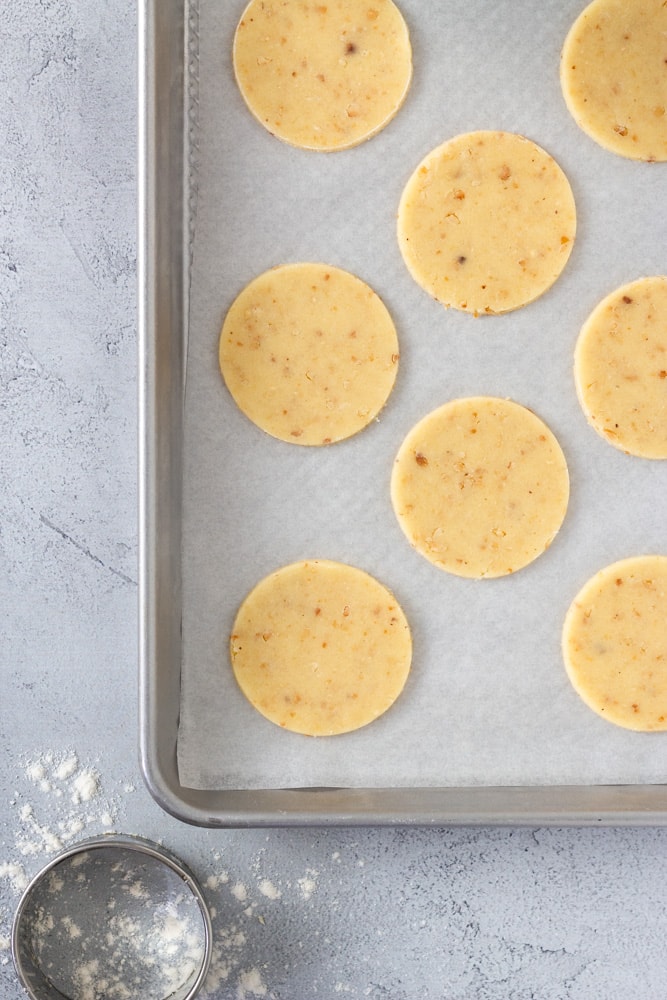 Overhead shot of a baking tray lined with parchment and topped with hazelnut cookie dough rounds with a round cutter in the corner.