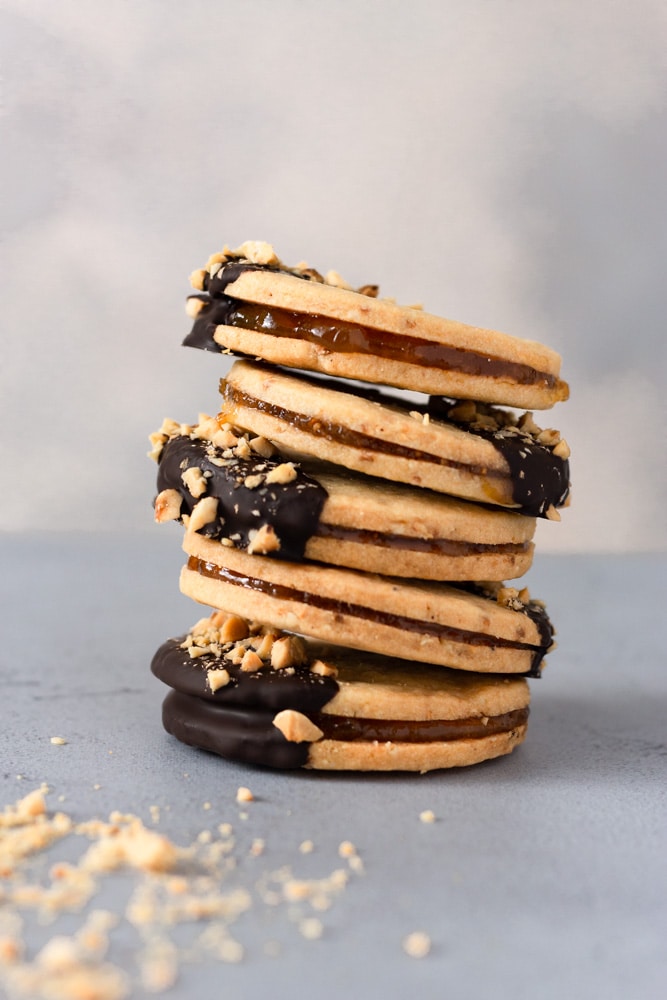 Straight on shot of a stack of Hazelnut Sandwich Cookies with Chocolate and Jam on a light blue grey surface with a light textured background.