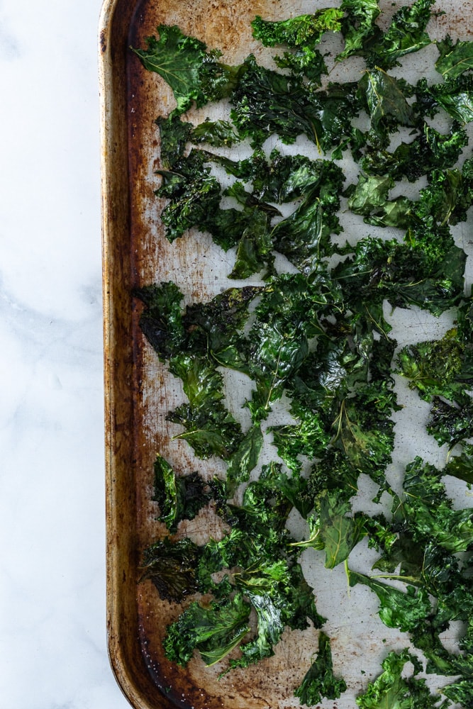 Overhead shot of a sheet tray of kale chips on a  marble surface.