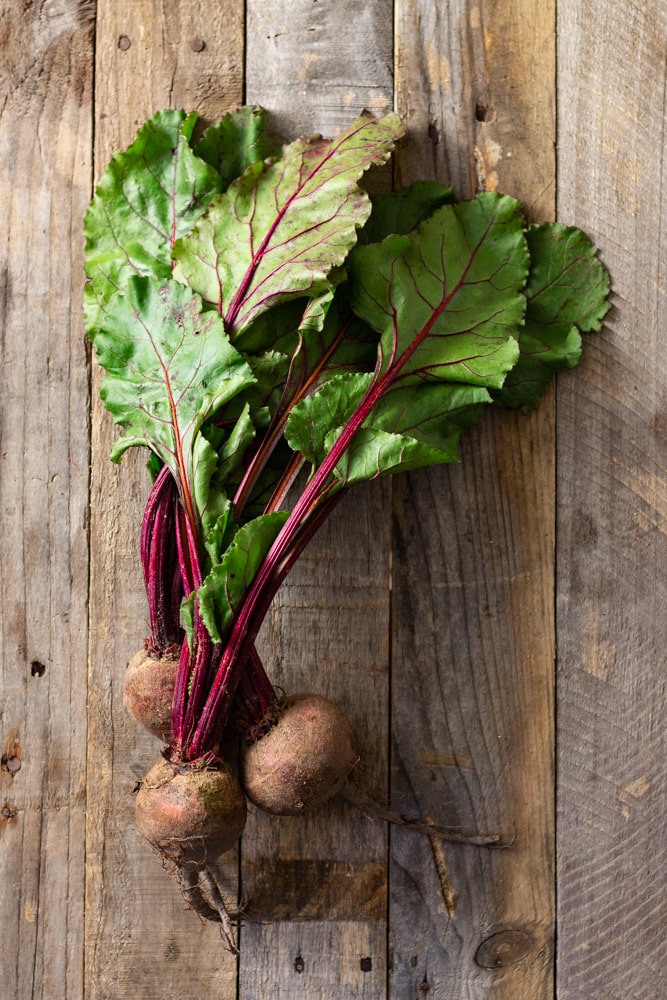 Overhead shot of fresh beets with greens on a rustic, grey wood surface.