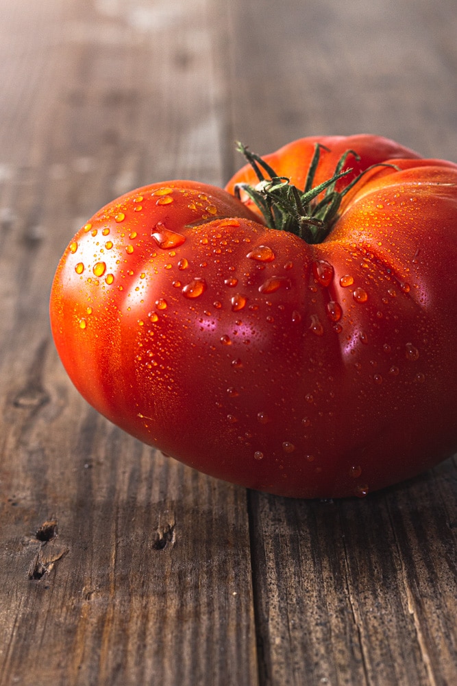 Straight on, close up shot of a large, red heirloom tomato with water droplets on it.