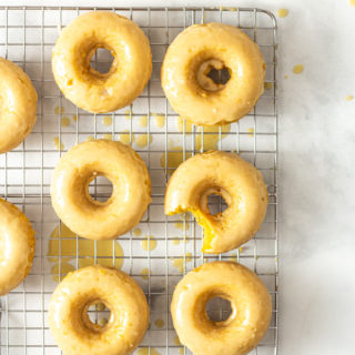 Baked pumpkin donuts with maple butter glaze on a cooling rack with white marble surface.
