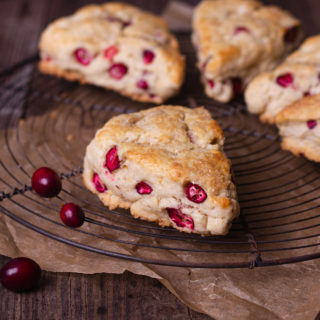 Straight on shot of Cranberry Orange Scones on a round wire rack on a rustic wood surface with a few fresh cranberries scattered around.
