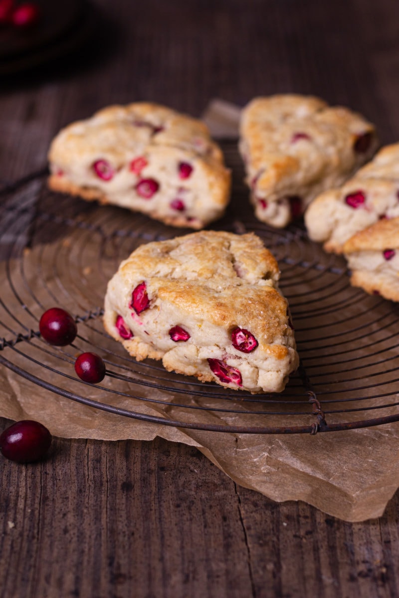 Straight on shot of Cranberry Orange Scones on a round wire rack on a rustic wood surface with a few fresh cranberries scattered around.