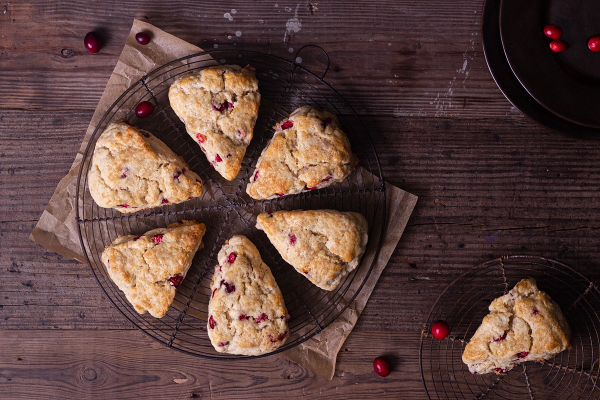 Overhead shot of Cranberry Orange Scones on a round wire rack on a rustic wood surface with a few fresh cranberries scattered around.