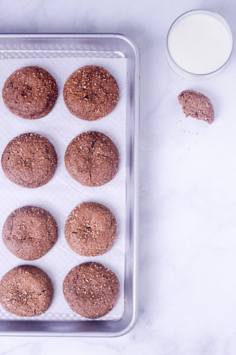 Chewy Ginger Molasses Cookies on a baking sheet, on a marble surface next to a glass of milk.