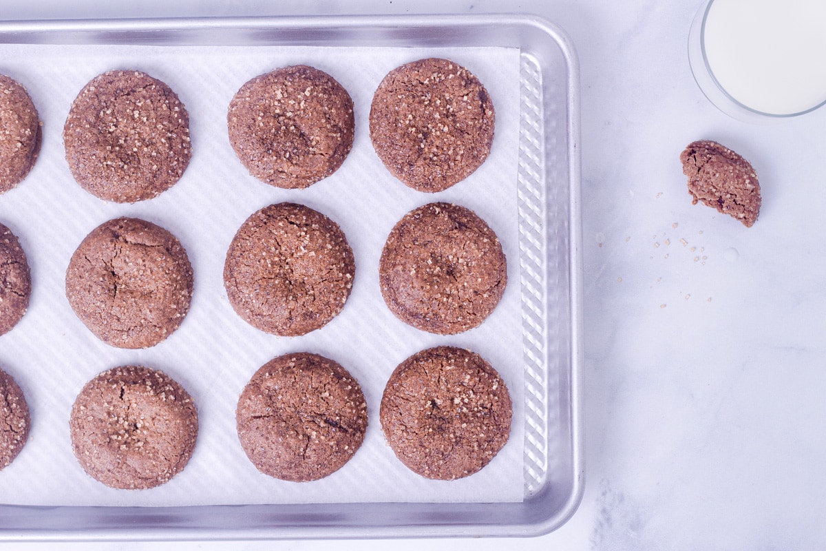 Chewy Ginger Molasses Cookies on a baking sheet, on a marble surface next to a glass of milk.