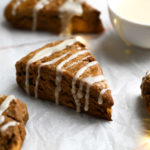 Gingerbread scones on parchment with Christmas lights and a bowl of lemon glaze.