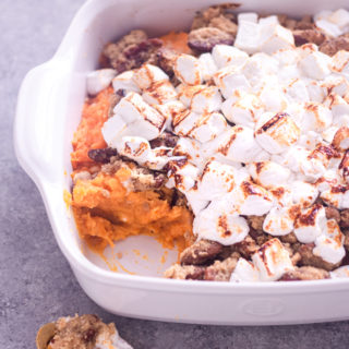 Angled view of sweet potato casserole with brown butter pecan topping and toasted mini marshmallows in a casserole dish.
