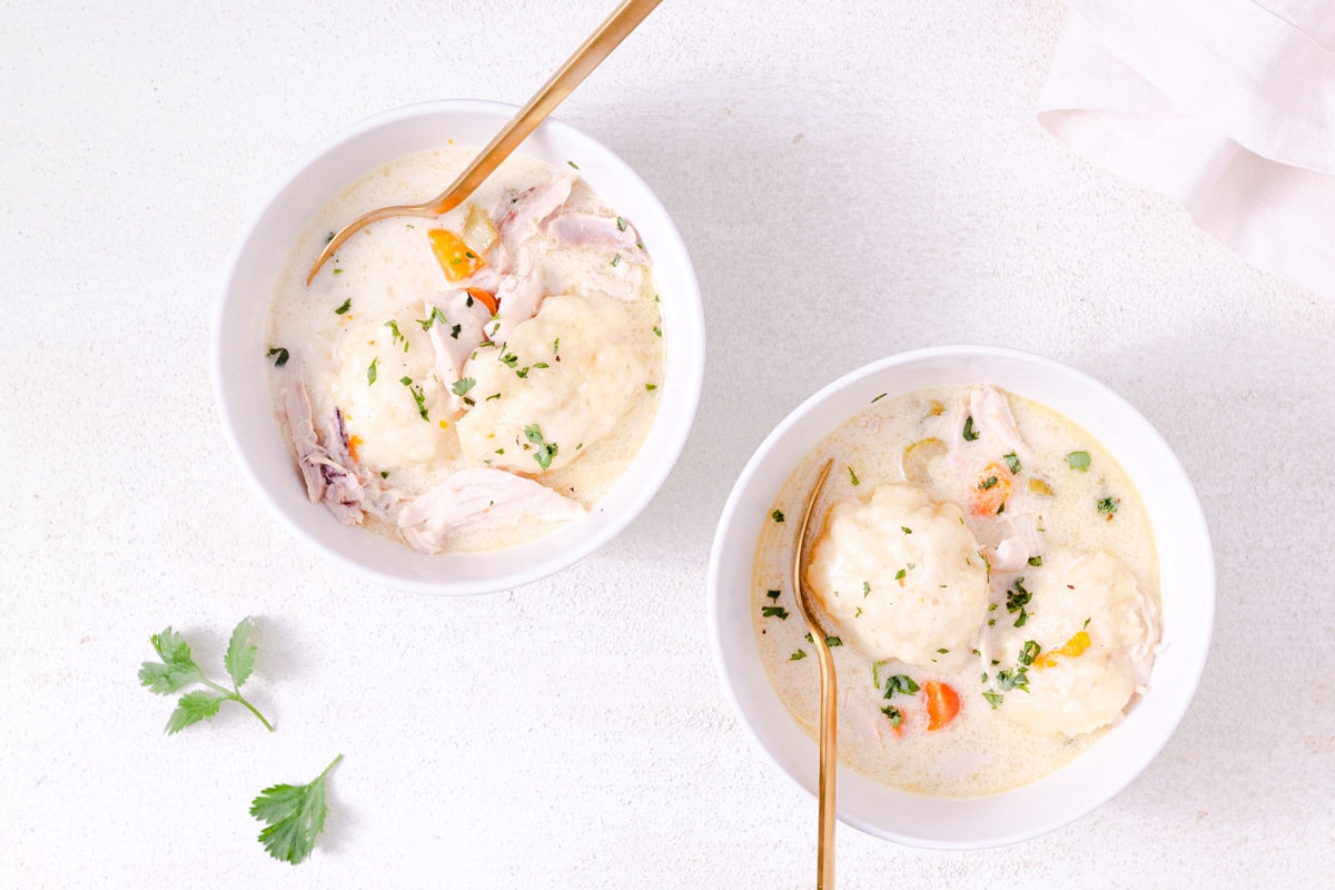 Chicken and Dumpling Soup in a white bowl with a gold spoon, another soup bowl in the background and a white surface.