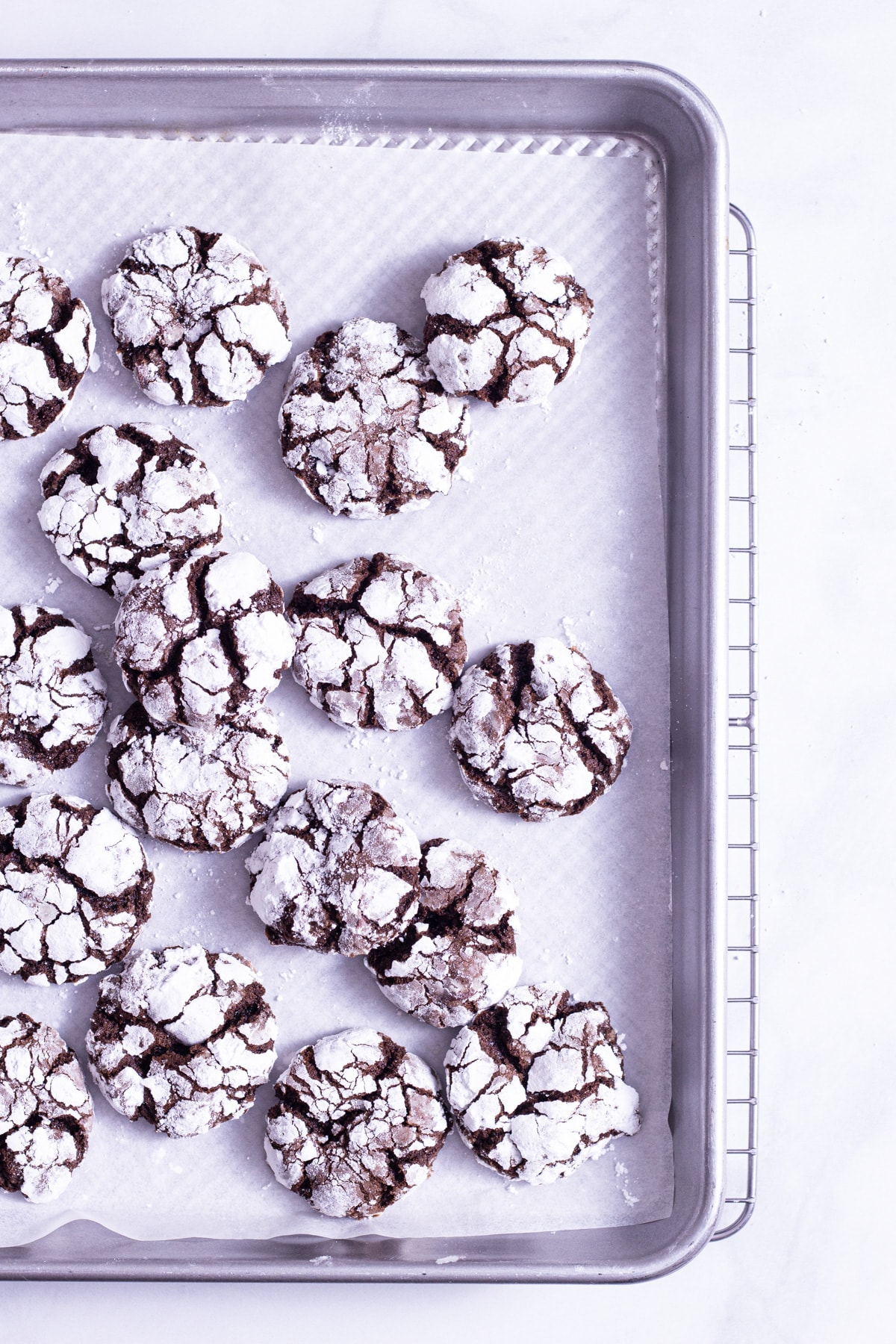 Overhead shot of Chocolate Crinkle Cookies scattered on a parchment lined baking sheet with a marble surface.