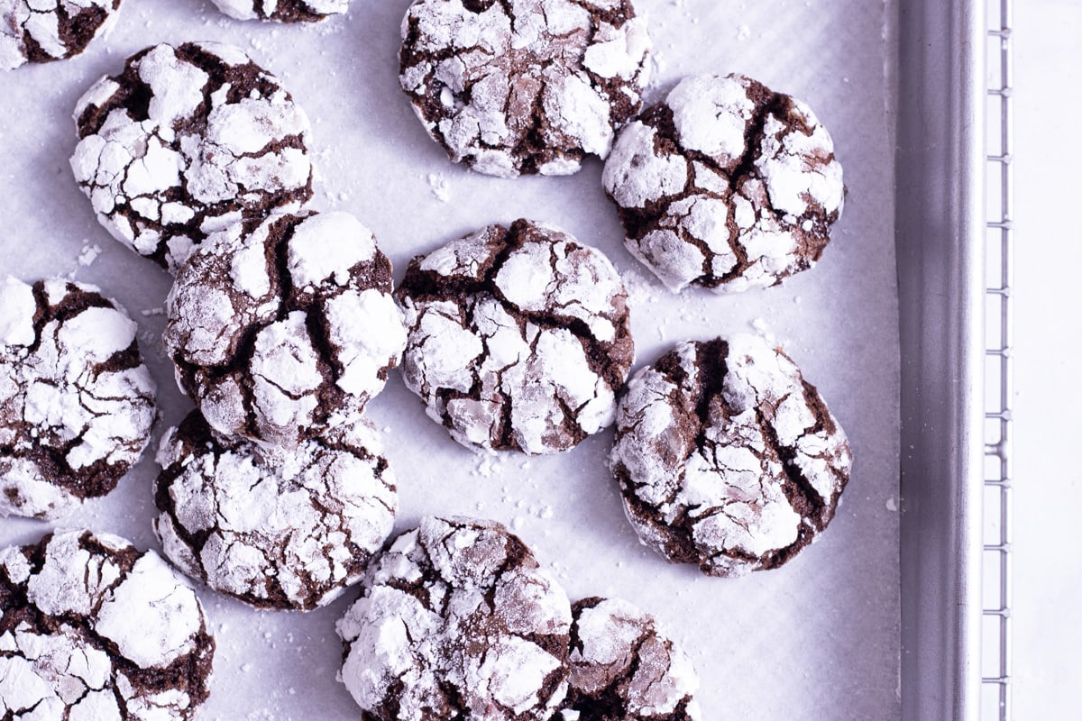 Overhead close up shot of Chocolate Crinkle Cookies scattered on a parchment lined baking sheet with a marble surface.