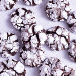 Overhead close up shot of Chocolate Crinkle Cookies scattered on parchment paper.