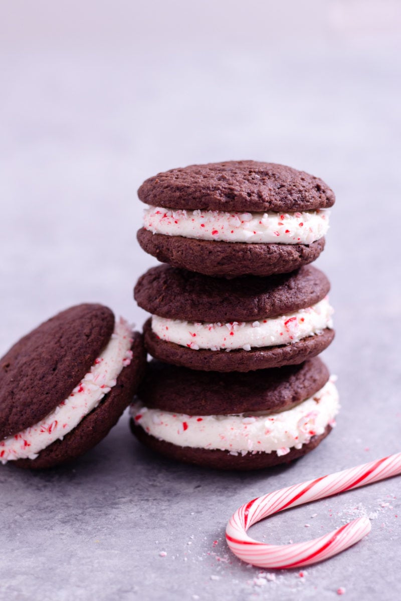 Straight on view of a stack of 3 Chocolate Peppermint Whoopie Pies with another whoopie pie leaning against the rest, next to a candy can with a light grey background.