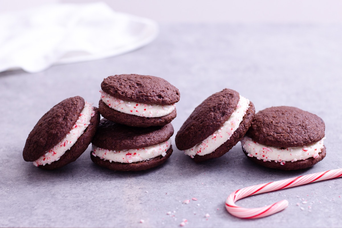 Straight on view of a row of stacked Chocolate Peppermint Whoopie Pies next to a candy cane with a light grey background.