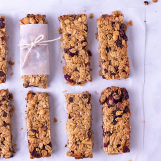 Overhead view of granola bars with walnuts, chocolate chips and dried cranberries lined up in two rows on a marble surface.