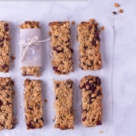 Overhead view of granola bars with walnuts, chocolate chips and dried cranberries lined up in two rows on a marble surface.
