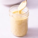 Close up straight on shot of Caesar Dressing in a jar with a spoon being dipped in.