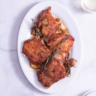 Overhead shot of a platter of Crispy Chicken Thighs with Rosemary and Garlic surrounded by glasses of wine and white plates on a marble surface.