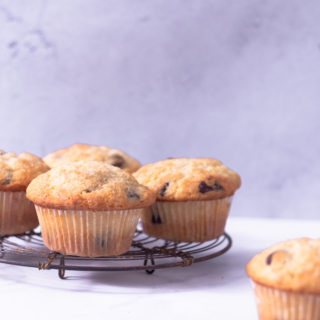 Straight on view of a cooling rack with Chocolate Chip Muffins on a white surface with a light blue background.