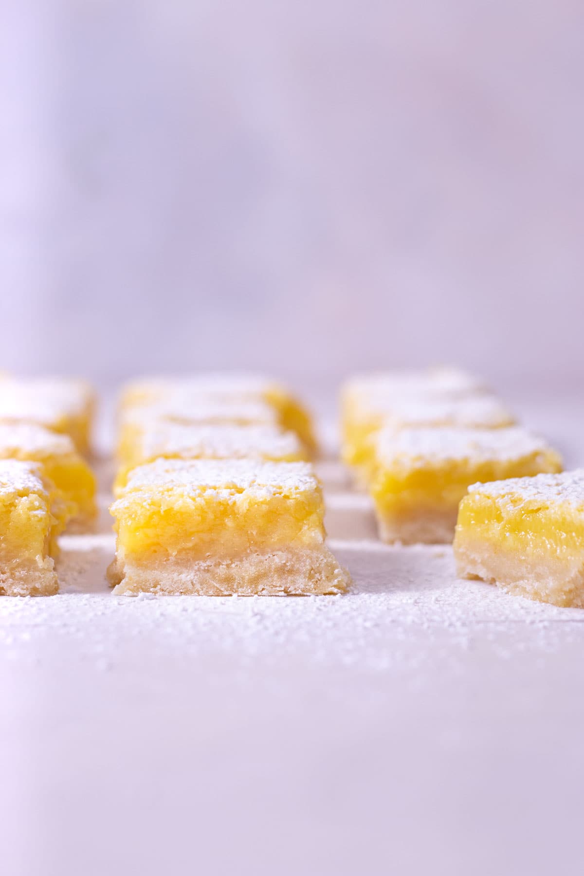 Straight on view of Lemon Bars lined up in a grid with a light blue background.