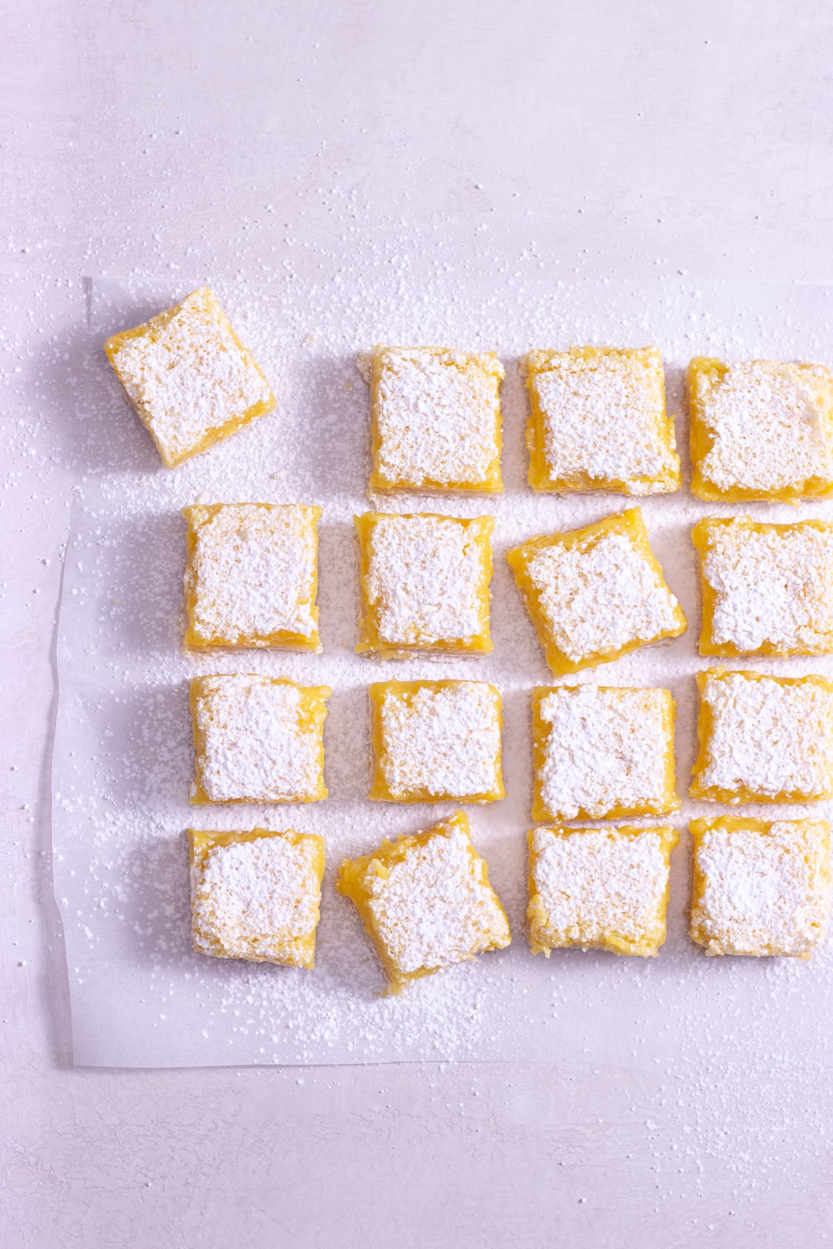 Overhead view of lemon squares on parchment on a light surface.
