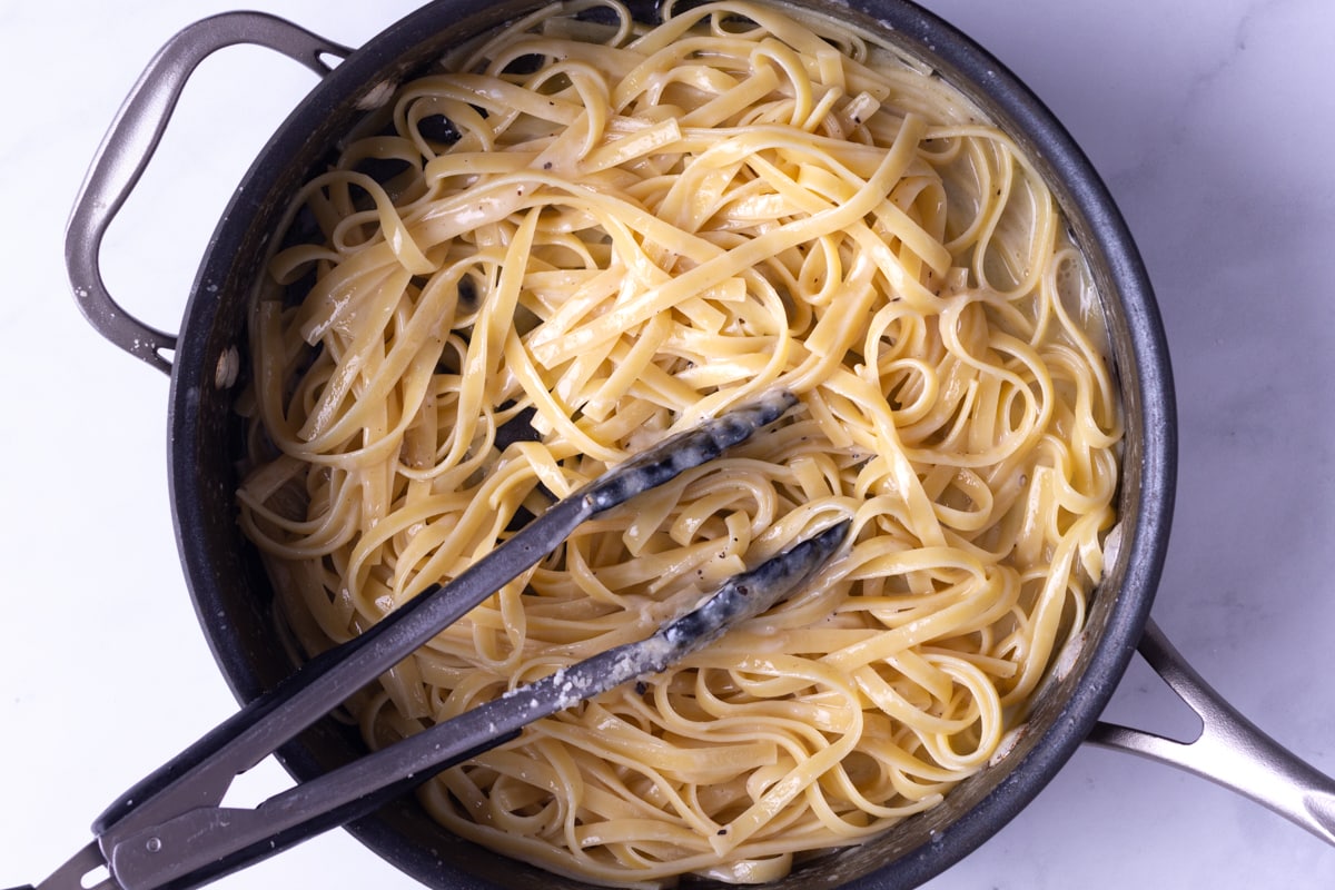 Overhead view of Fettuccine Alfredo Pasta in a pan with tongs.