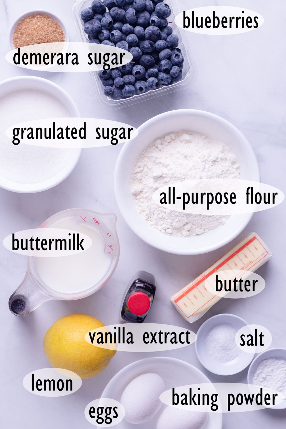 Overhead view of ingredients for blueberry muffins, including flour, buttermilk, butter, sugar and eggs.