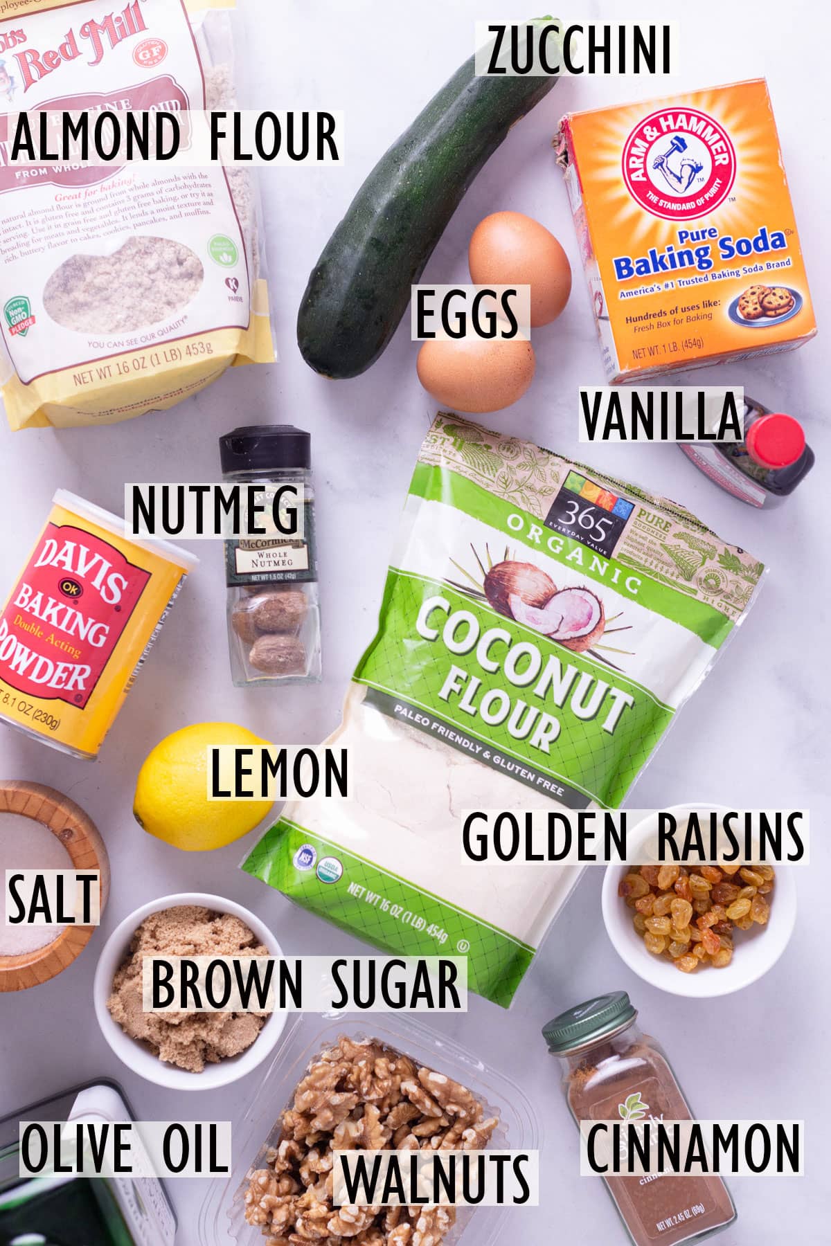 Individual ingredients needed for zucchini bread, including almond flour, coconut flour, zucchini, eggs, brown sugar, walnuts and raisins.