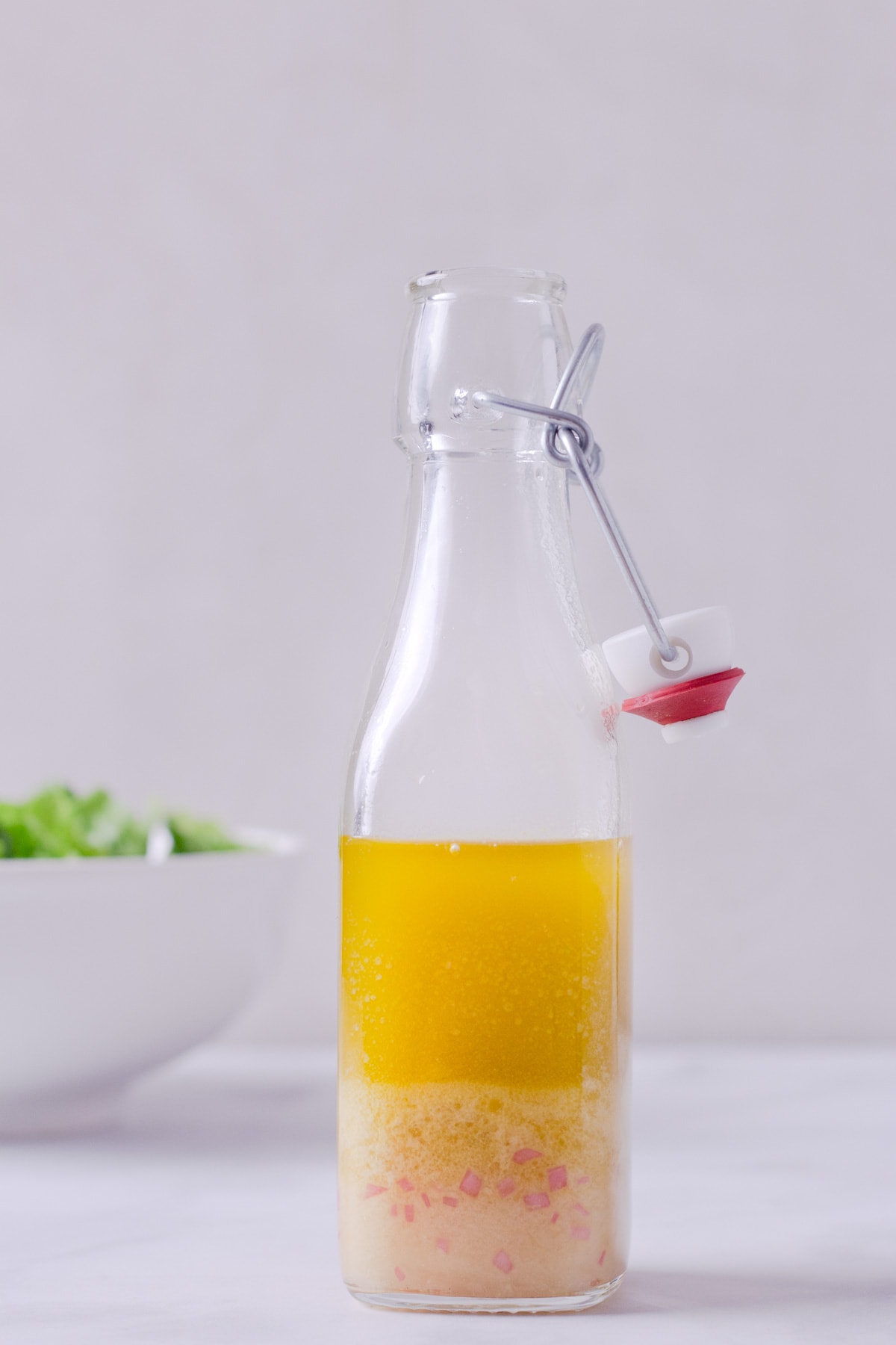 Straight on view of a bottle of Apple Cider Vinegar Dressing with a salad in the background.