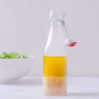 Straight on view of a bottle of Apple Cider Vinegar Dressing with a salad in the background.