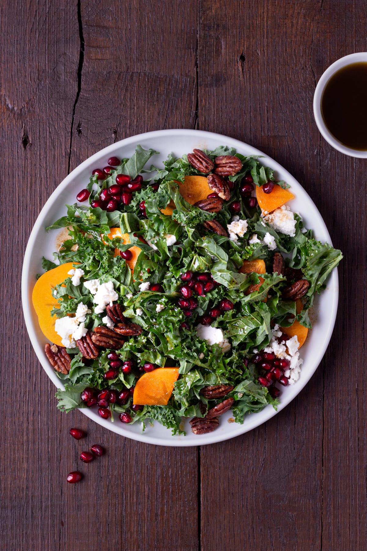 Overhead shot of a plate of kale salad with pomegranates, persimmons, pecans and feta cheese.