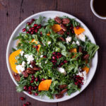 Overhead shot of a plate of kale salad with pomegranates, persimmons, pecans and feta cheese.