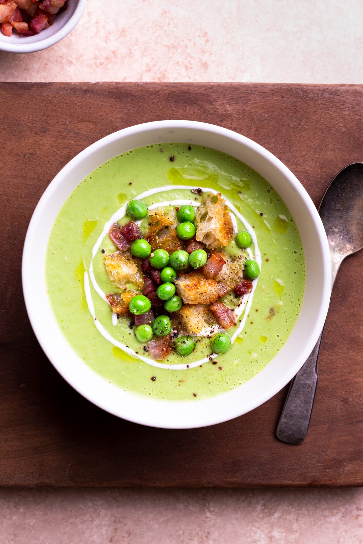 Closeup overhead view of a bowl of Green Pea Soup topped with yogurt, pancetta, peas and croutons.
