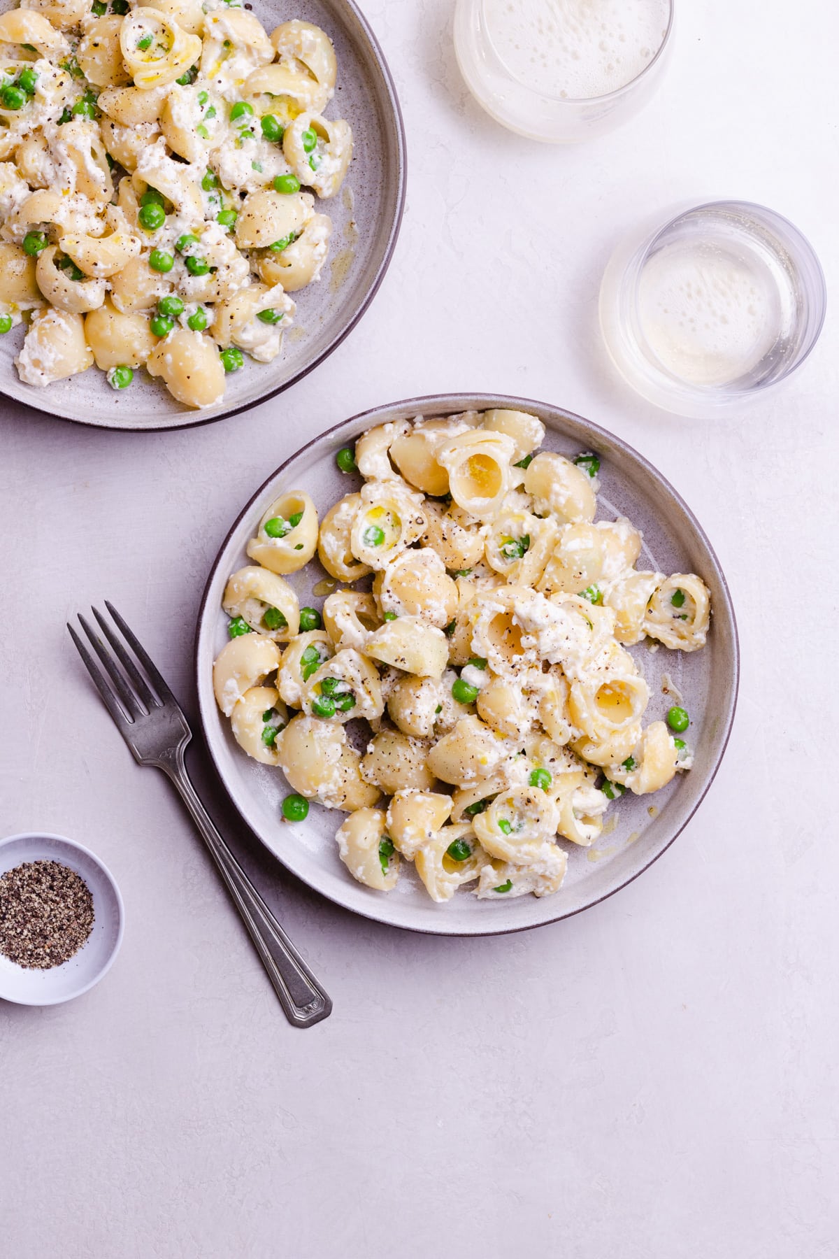 Overhead view of two bowls of pasta with ricotta and peas topped with olive oil and black pepper.