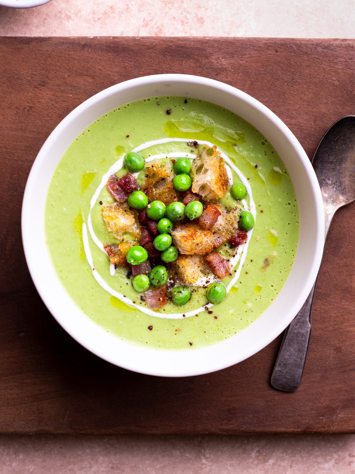 Overhead image of a bowl of creamy green pea soup topped with pancetta and croutons.