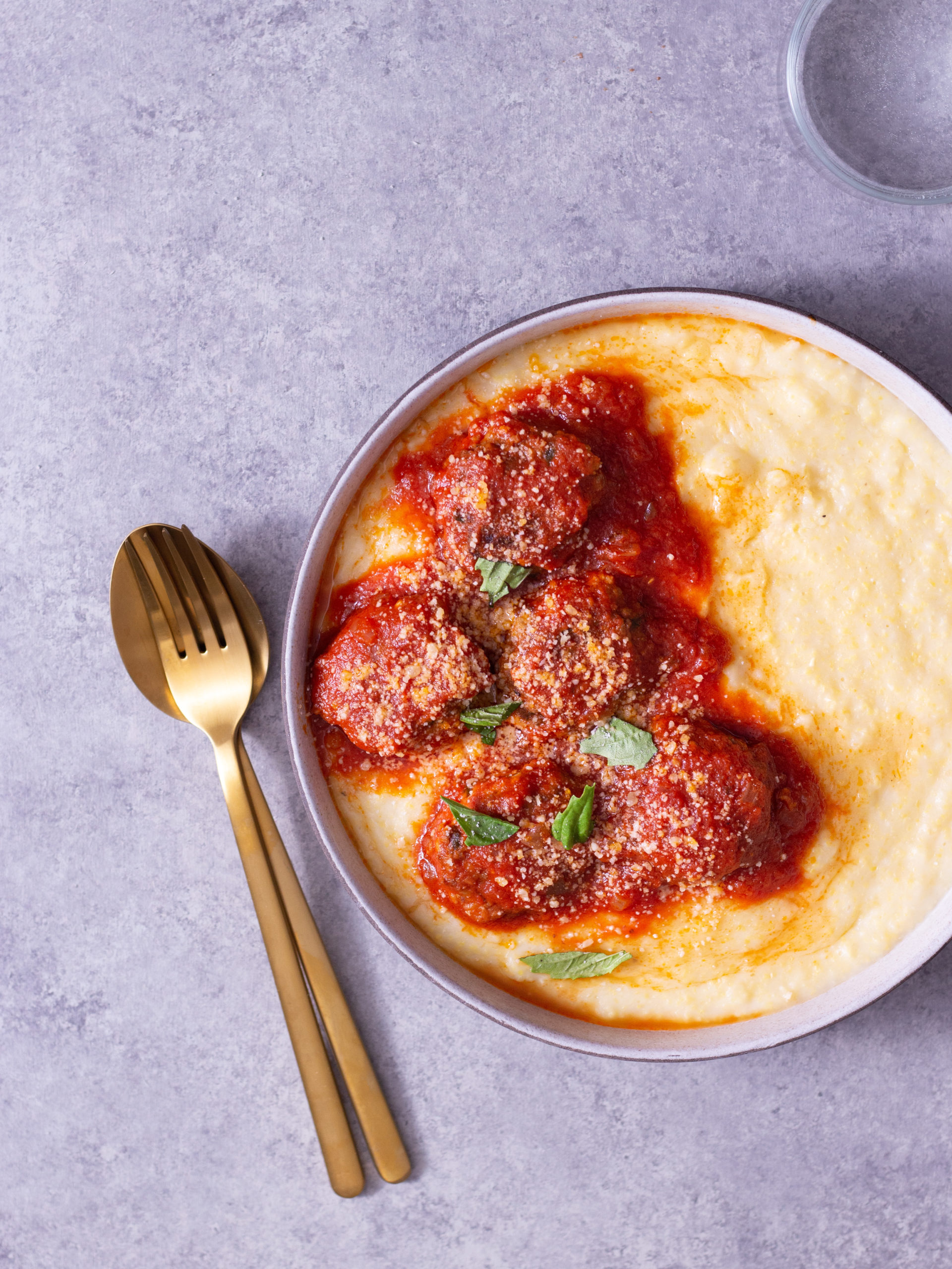 Instant Pot Meatballs in a bowl over polenta on a light grey textured surface.