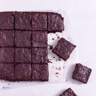 Avocado Brownies cut into squares on a cream surface near a glass of milk.