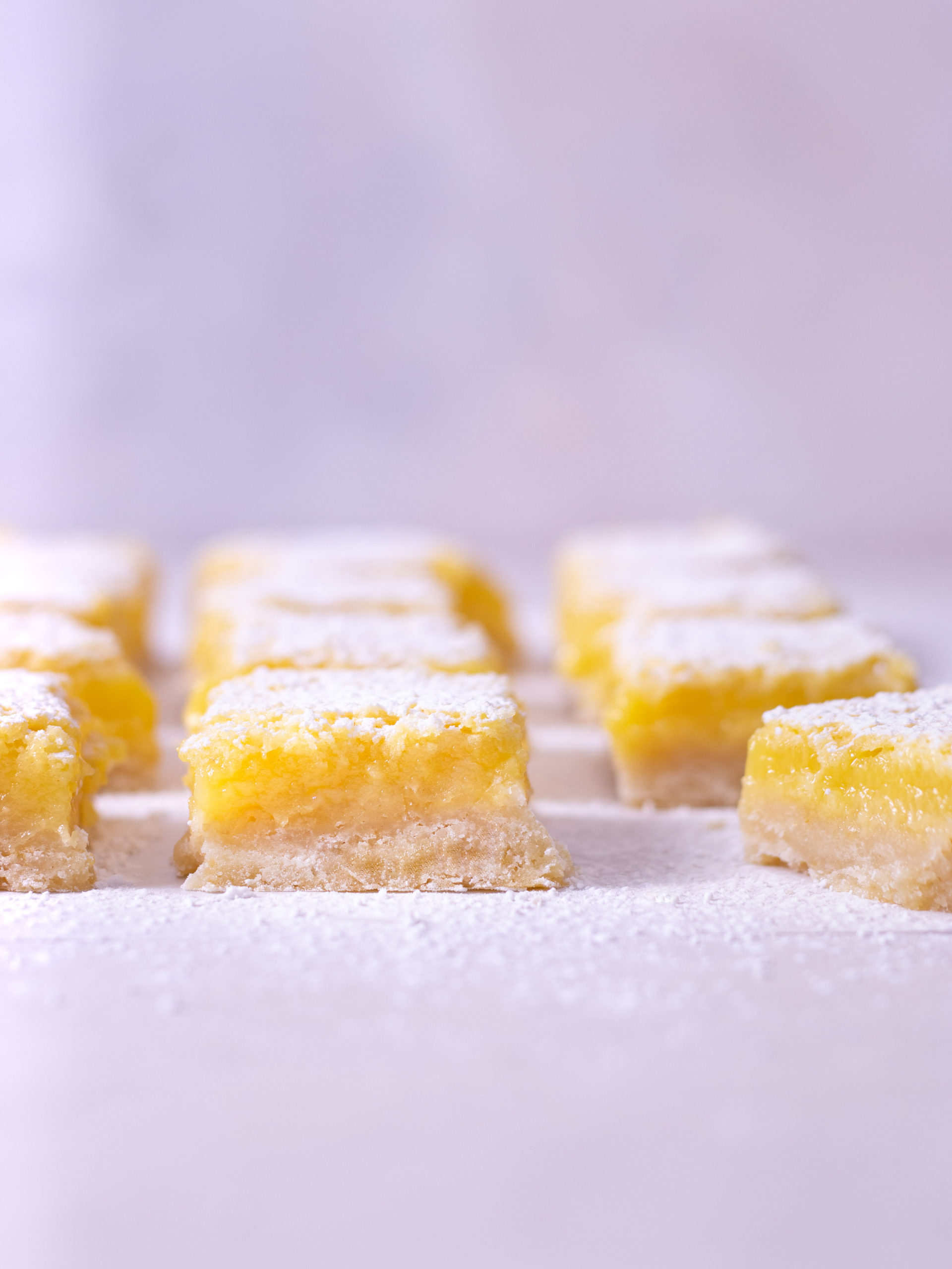 Straight on shot of rows of lemon bars on a light surface.