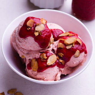 Strawberry Balsamic Ice Cream in a bowl topped with strawberry sauce and toasted almonds.